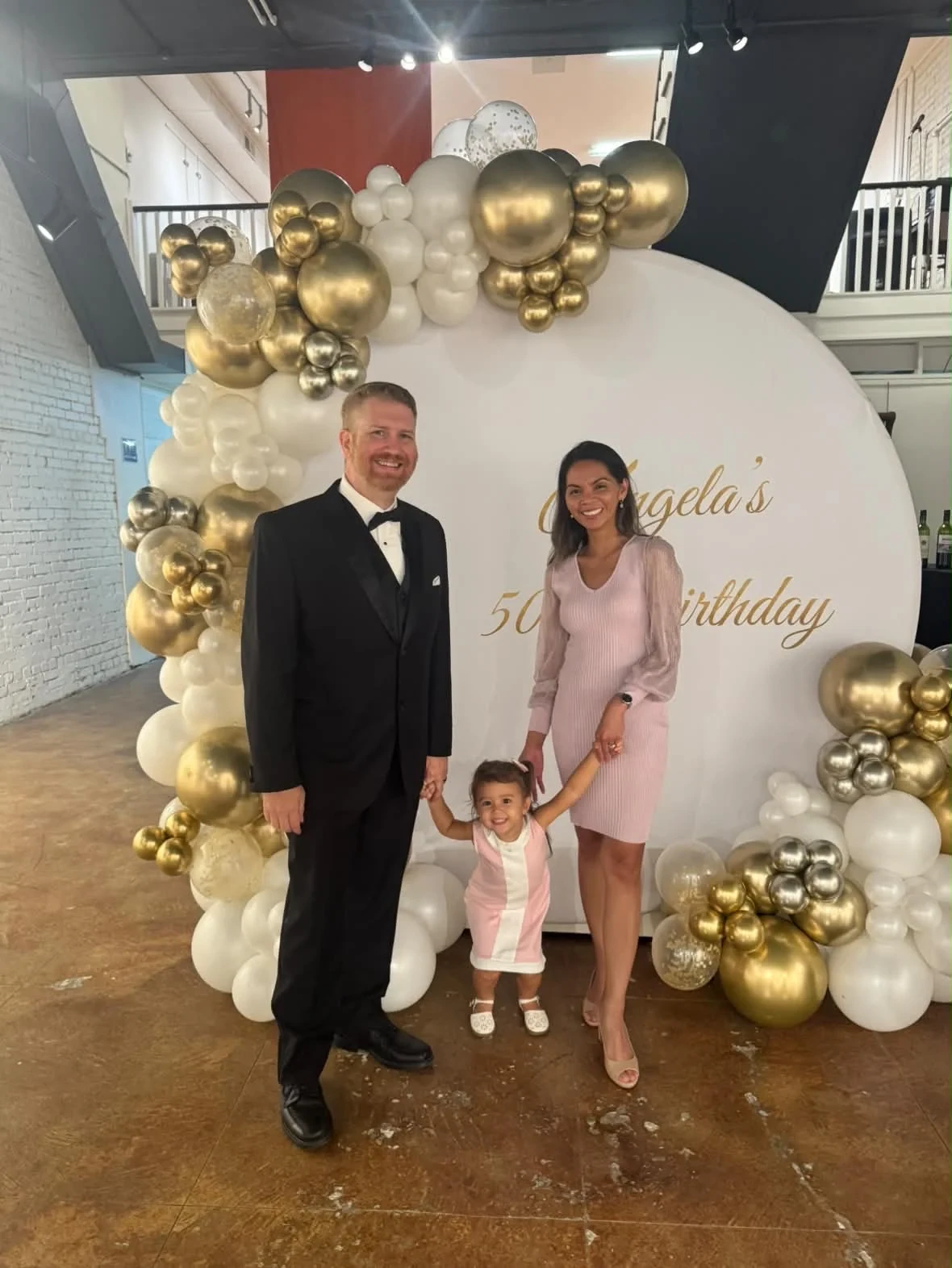 Two adults and a child posing at the birthday backdrop.