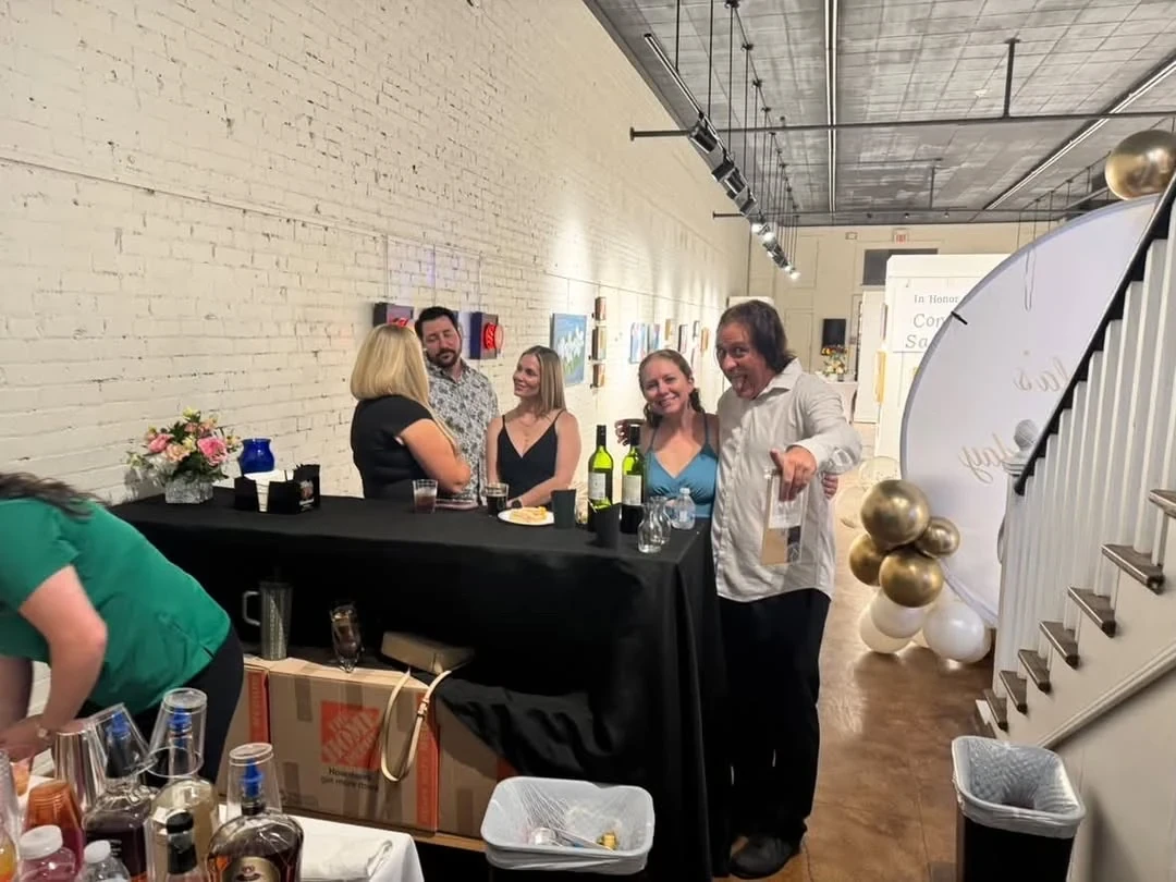 Guests smiling and visiting beside the bar and balloon backdrop.