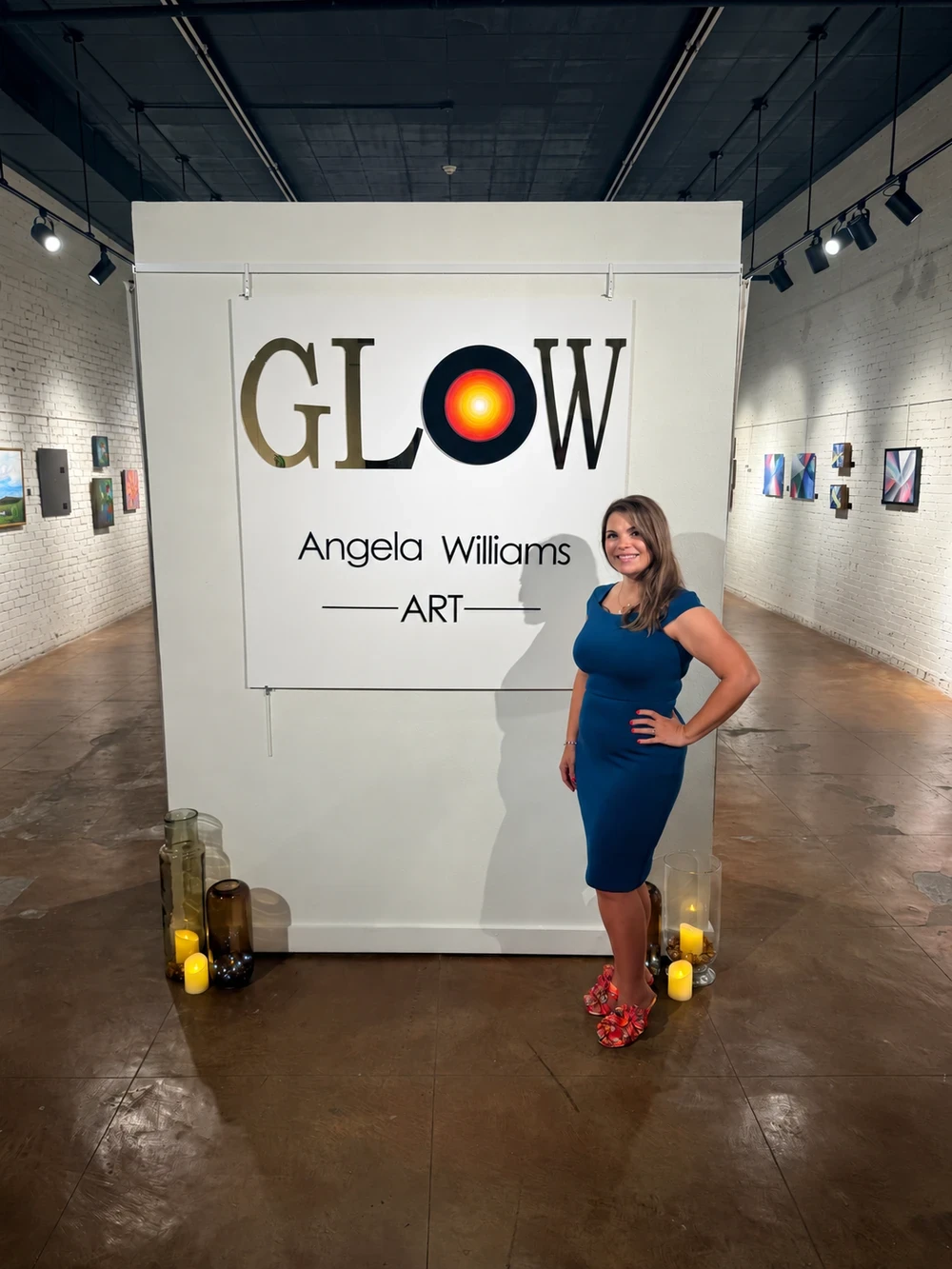 Angela Williams beside the GLOW exhibition sign in the gallery.