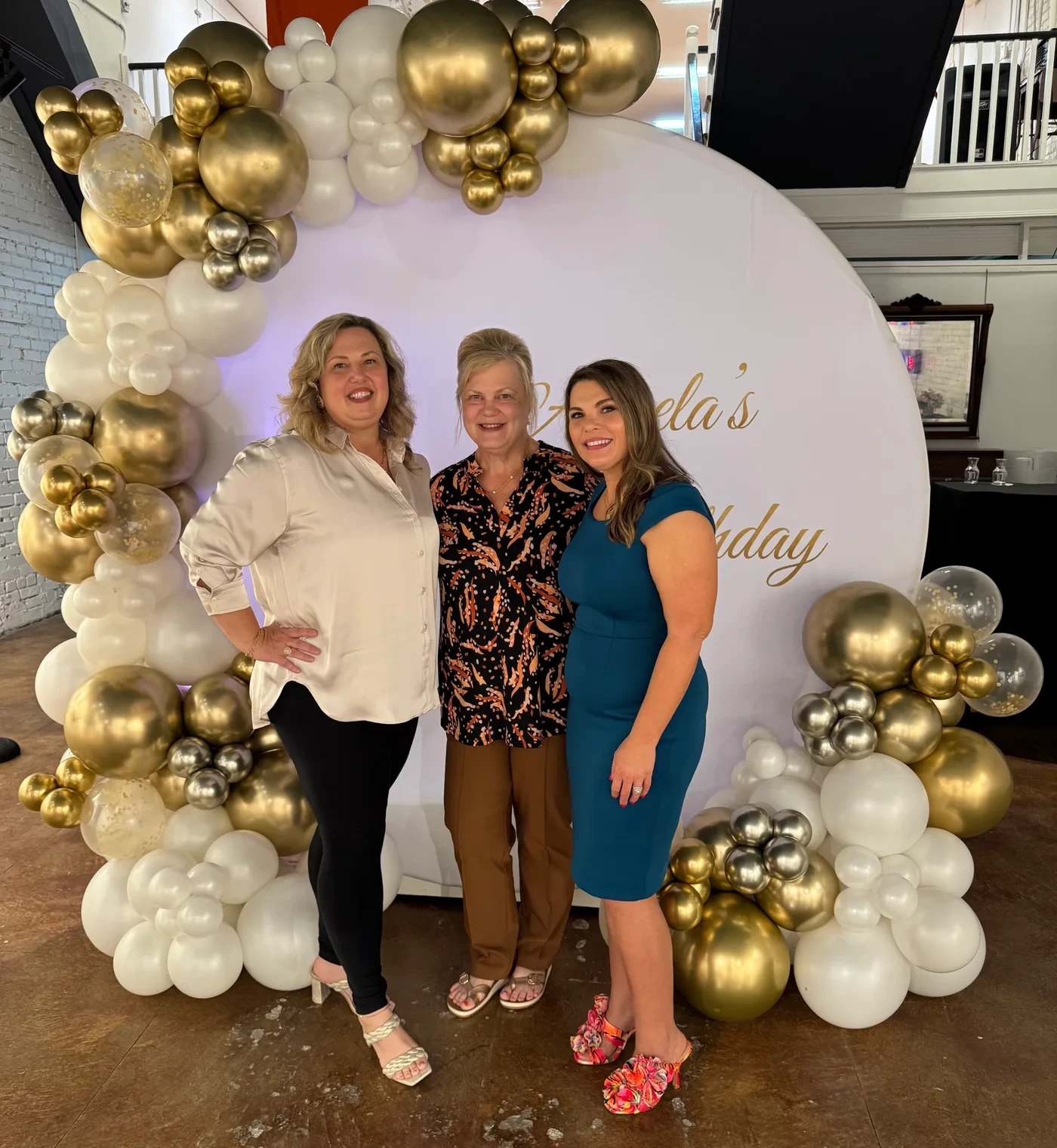Three women posing together at the birthday backdrop.