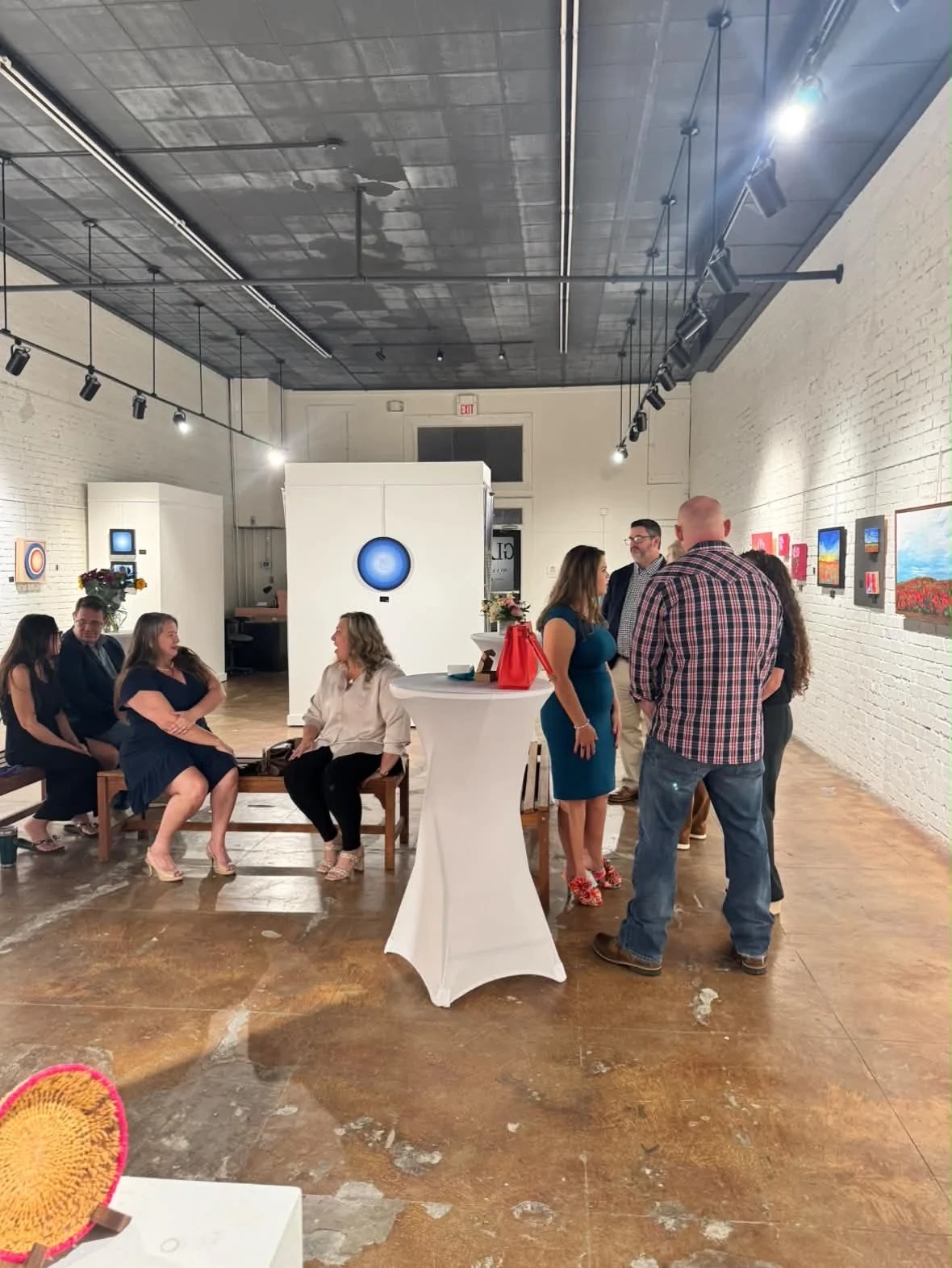 Guests talking and seated among paintings and white cocktail tables.