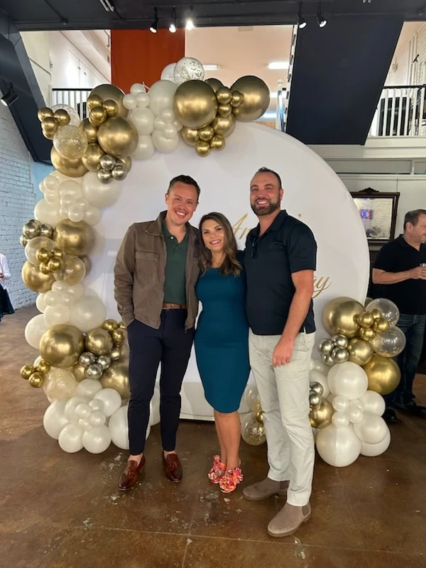 Angela posing with two guests at the gold and white birthday backdrop.