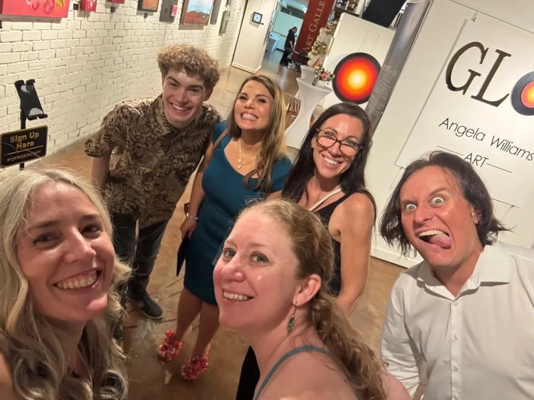 A group of guests taking a playful selfie beside the GLOW sign.