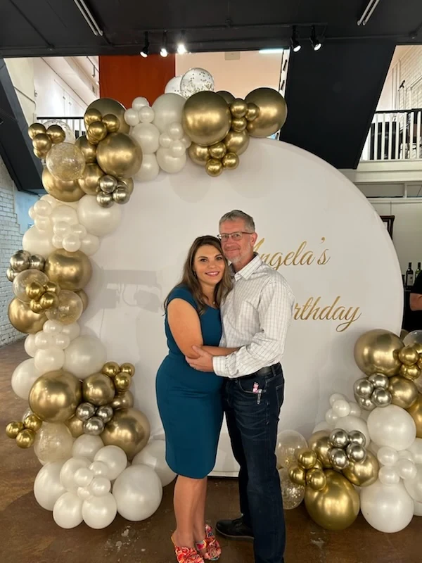Angela and a guest posing together beside the birthday balloons.