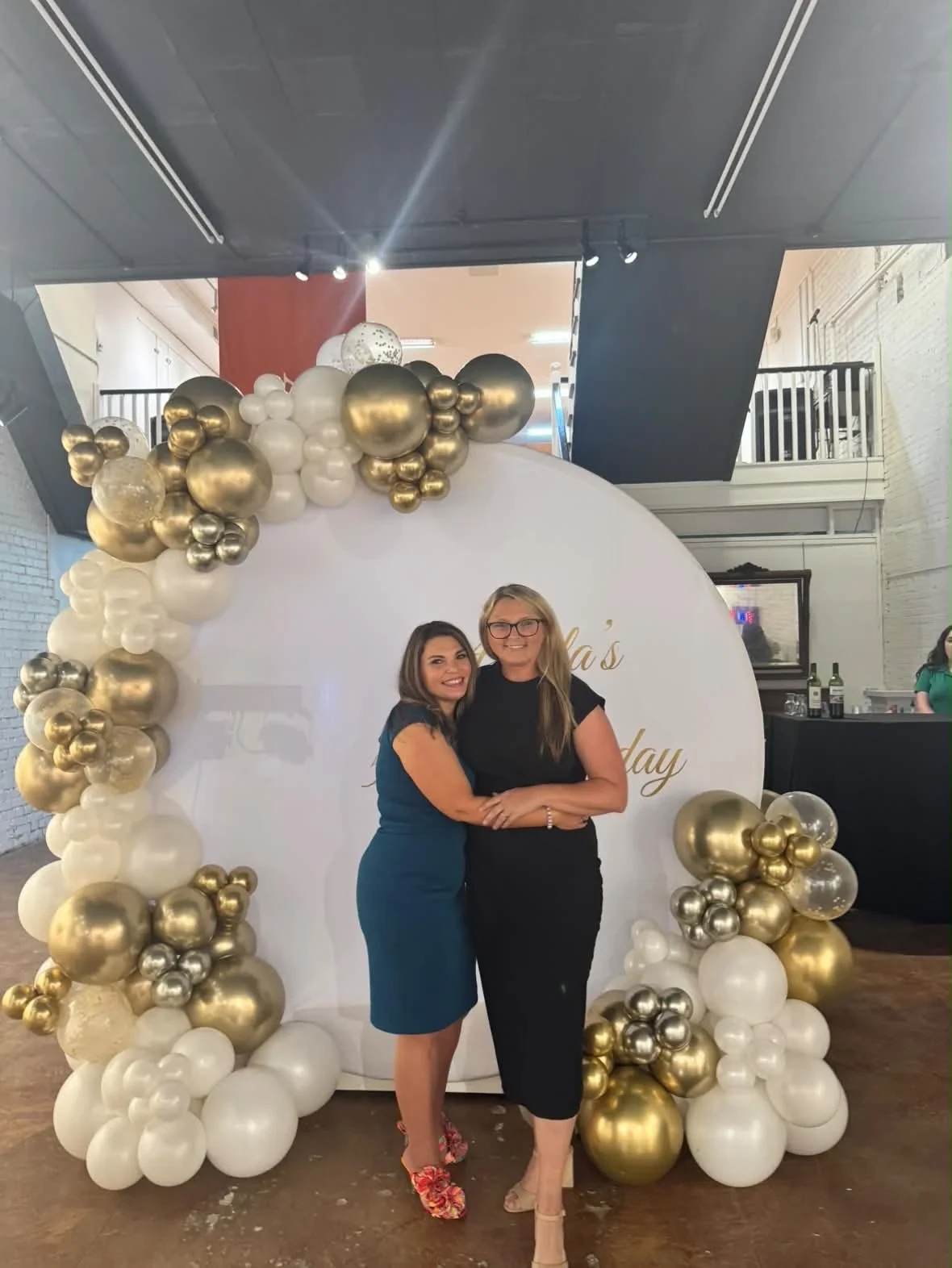 Two women posing together beside the birthday balloons.