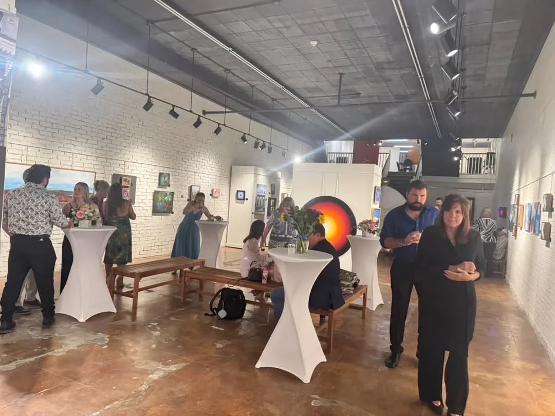 A view across the gallery with guests, artwork and flowers.