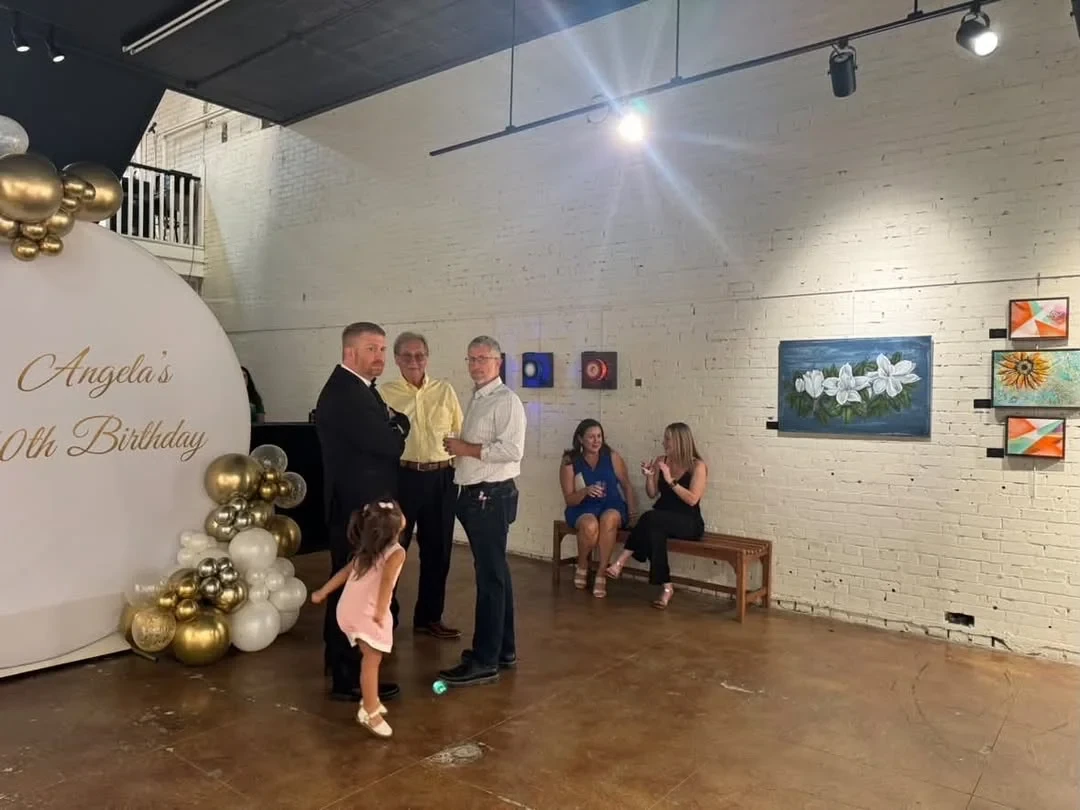 Guests visiting near the birthday backdrop and a floral painting.