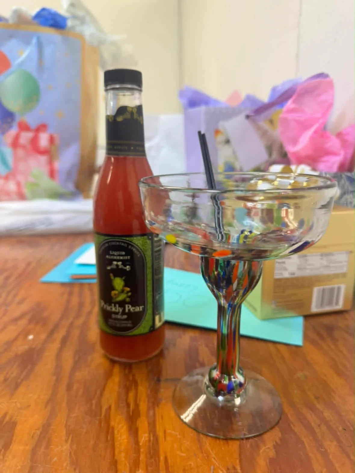 A decorative cocktail glass and a bottle of prickly pear mixer beside gifts.