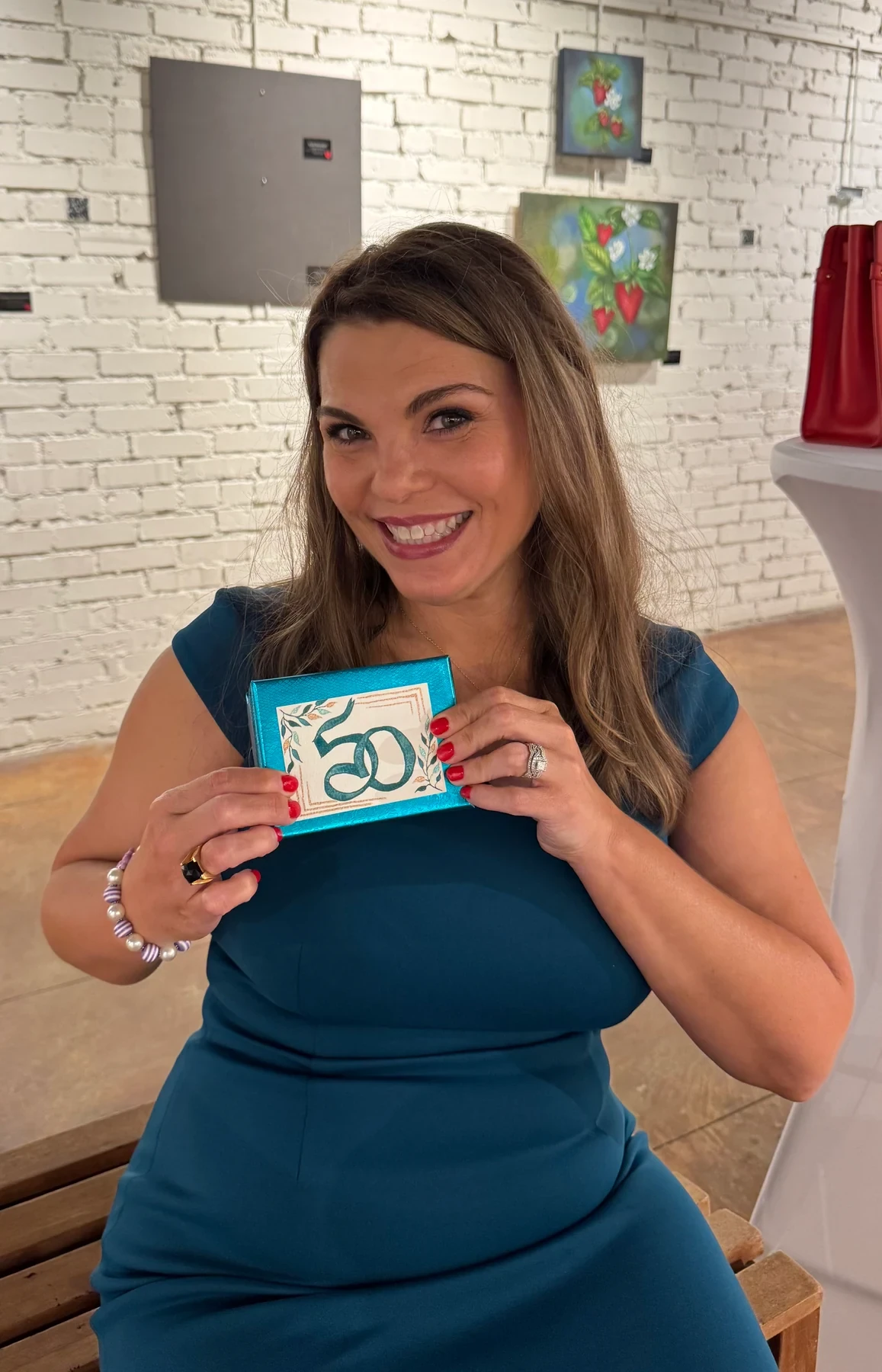 Angela holding a turquoise birthday card marked 50.