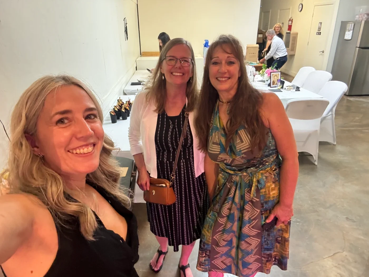 Three guests smiling together near the refreshment tables.